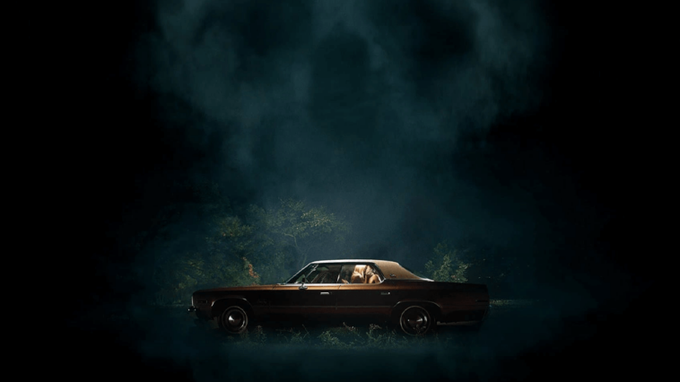 Promotional image for the film, It Follows, featuring a car with two people inside, centered in frame, on a dark night.